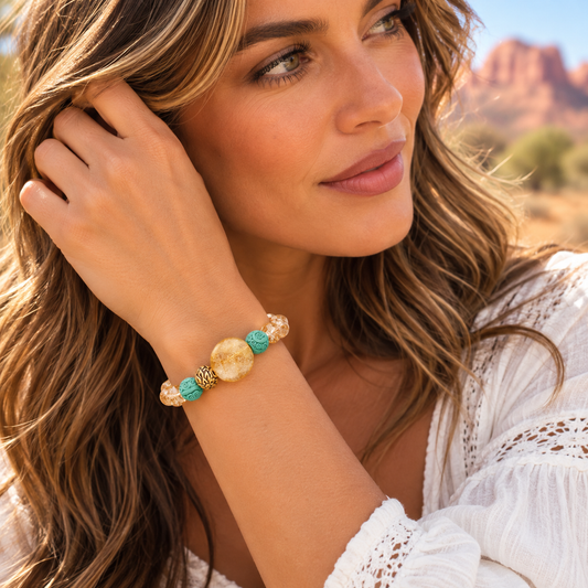 A woman wearing a bohemian-style beaded bracelet with turquoise, cream, and gold beads, photographed outdoors against a desert canyon background.