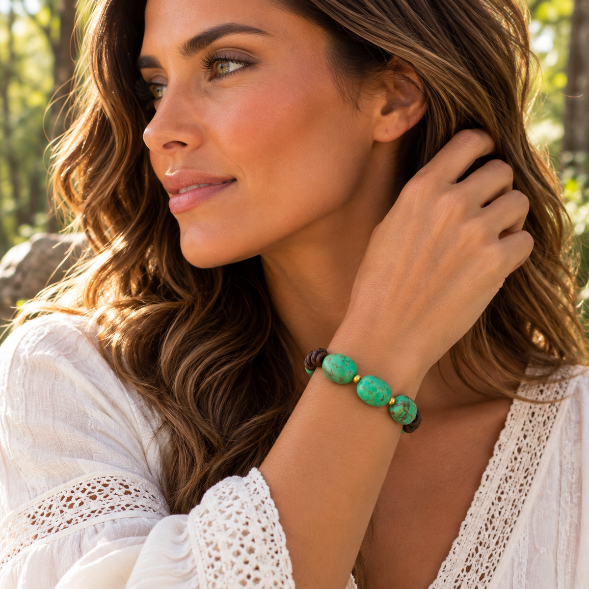 A woman wearing a beaded bracelet with green and white marbled beads and small gold accents, photographed outdoors in a sunlit natural setting.