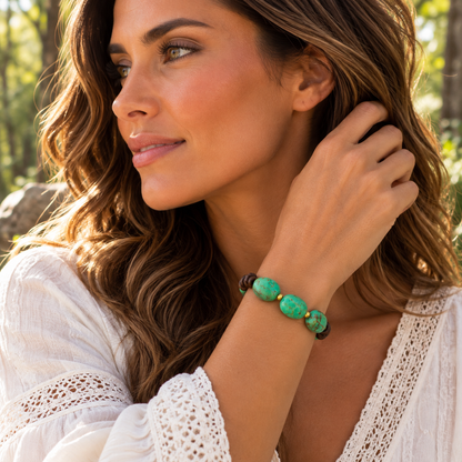 A woman wearing a beaded bracelet with green and white marbled beads and small gold accents, photographed outdoors in a sunlit natural setting.