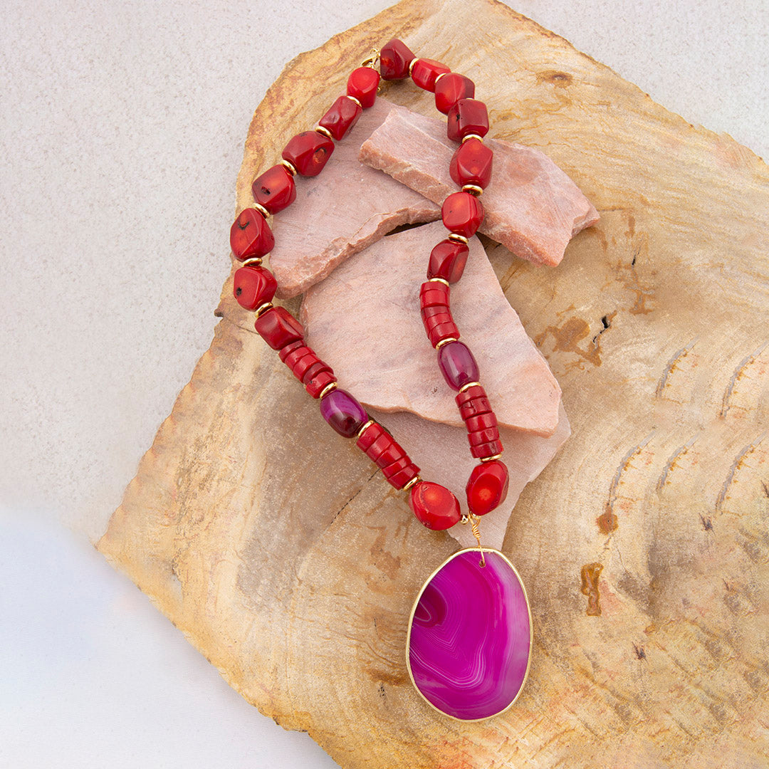 Necklace with red beads and a pink pendant on a textured stone surface