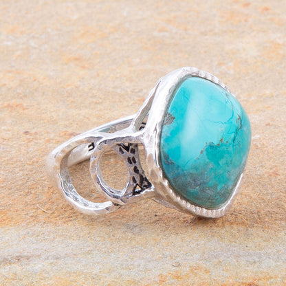 Turquoise ring with silver band on a beige stone background