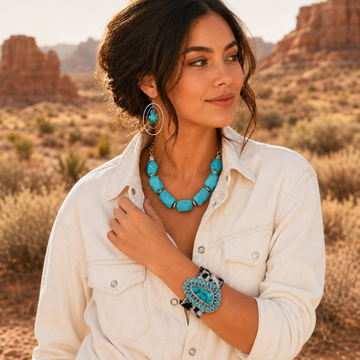A woman in a desert landscape wearing a turquoise statement necklace, matching drop earrings, and a turquoise-and-black cuff bracelet.