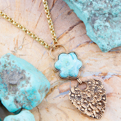 Necklace with turquoise flower pendant and gold heart-shaped charm on a stone background