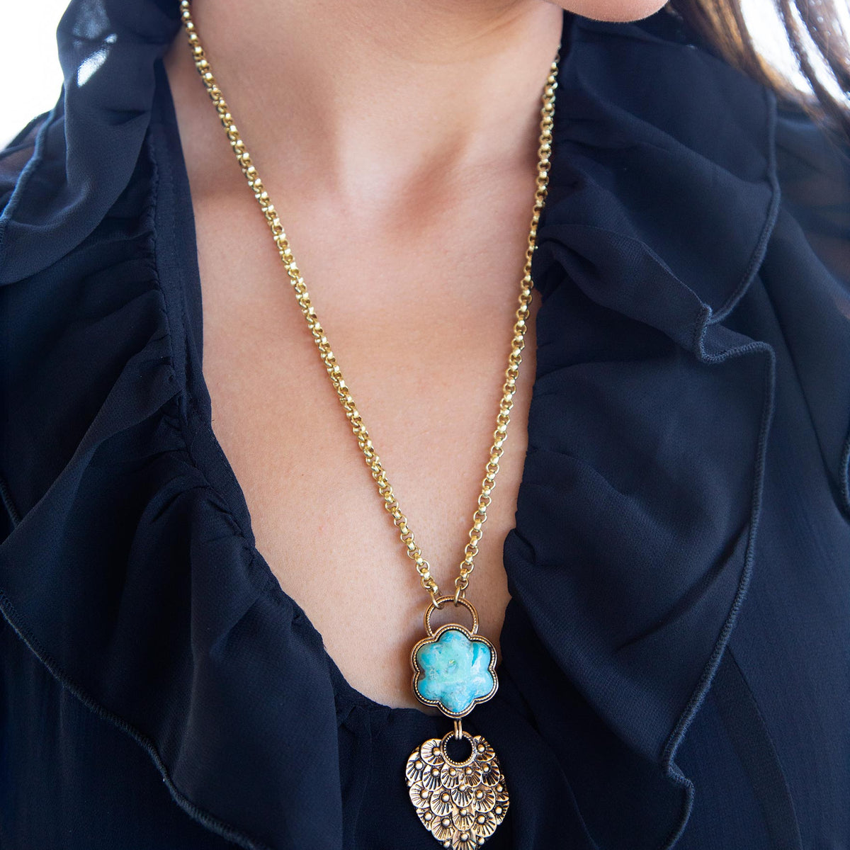 Gold necklace with a blue pendant worn by a person in a dark blue outfit.