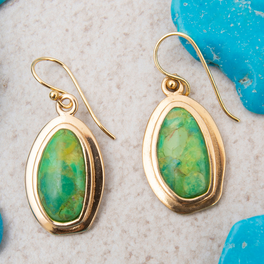 Gold earrings with green stones on a textured surface