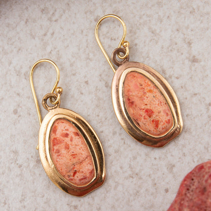 Pair of gold earrings with pink stone on a textured surface