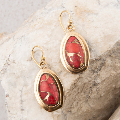 Gold earrings with red stone on a marble surface