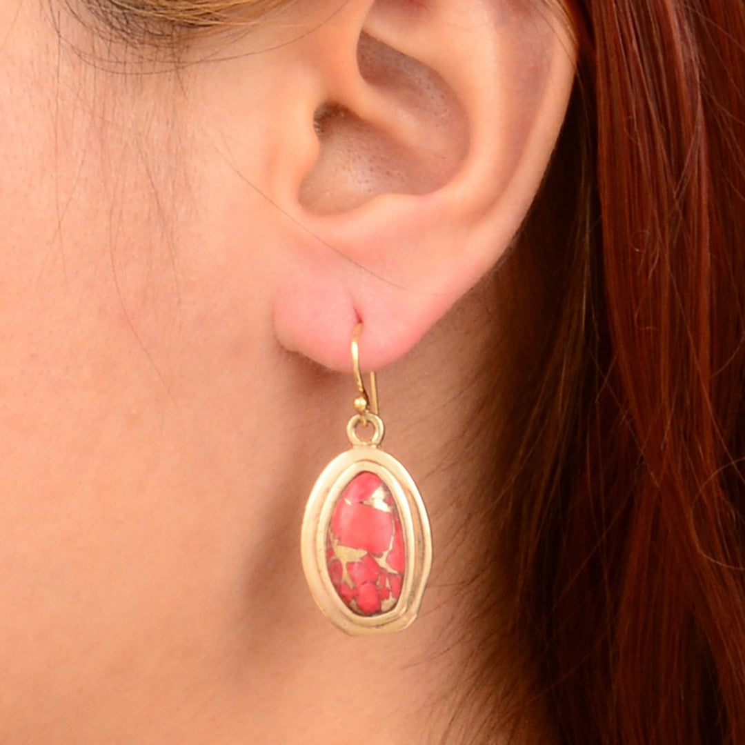 Gold earring with a red stone worn by a person with red hair.