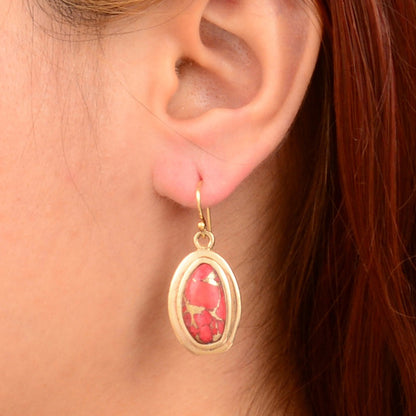 Gold earring with a red stone worn by a person with red hair.