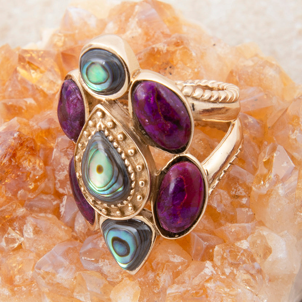 Gold ring with purple and green gemstones on a crystal background