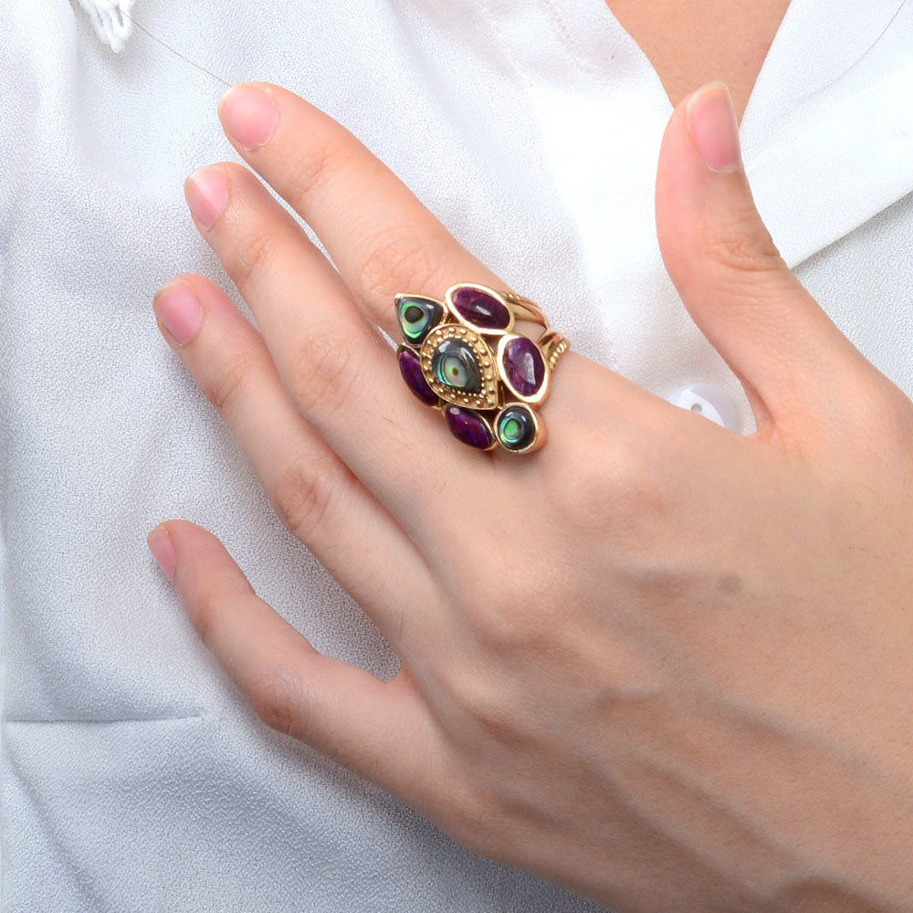 Hand wearing a ring with multicolored gemstones on a white background