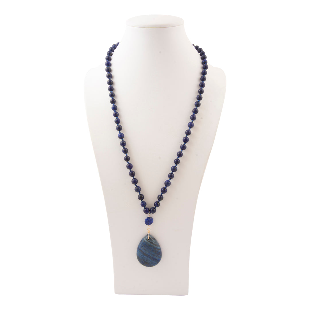 A beaded necklace with dark blue lapis lazuli-style round beads and a larger teardrop-shaped blue stone pendant, displayed on a white mannequin bust against a white background.