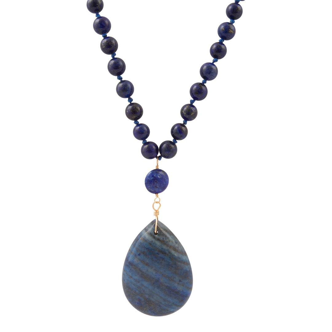 A beaded necklace featuring dark blue lapis lazuli round beads, a small matching blue bead, and a large teardrop-shaped blue stone pendant with natural banding, suspended from gold-toned rings.
