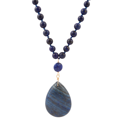 A beaded necklace featuring dark blue lapis lazuli round beads, a small matching blue bead, and a large teardrop-shaped blue stone pendant with natural banding, suspended from gold-toned rings.