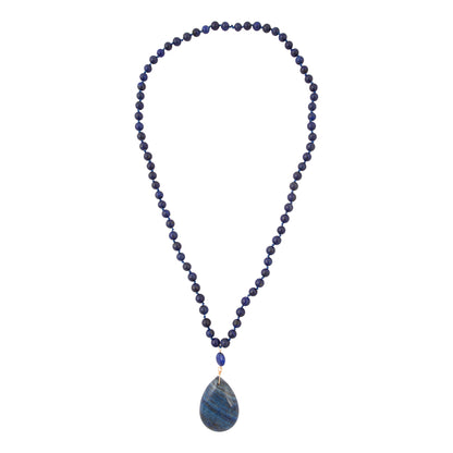 A beaded necklace featuring dark blue lapis lazuli stones, with a teardrop-shaped blue stone pendant and a small gold accent bead, shown against a plain white background.