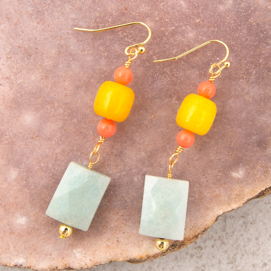 Pair of earrings with yellow, orange, and green beads on a stone surface