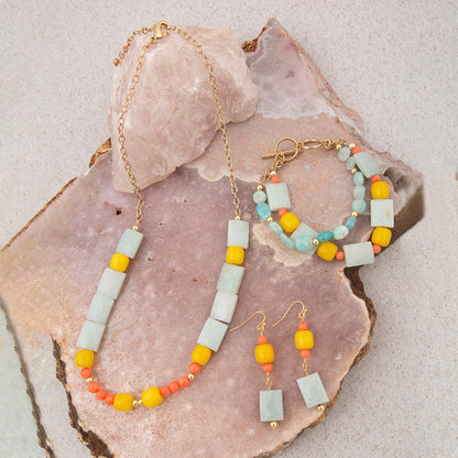 Jewelry set with necklace, hoop earrings, and drop earrings on a stone surface