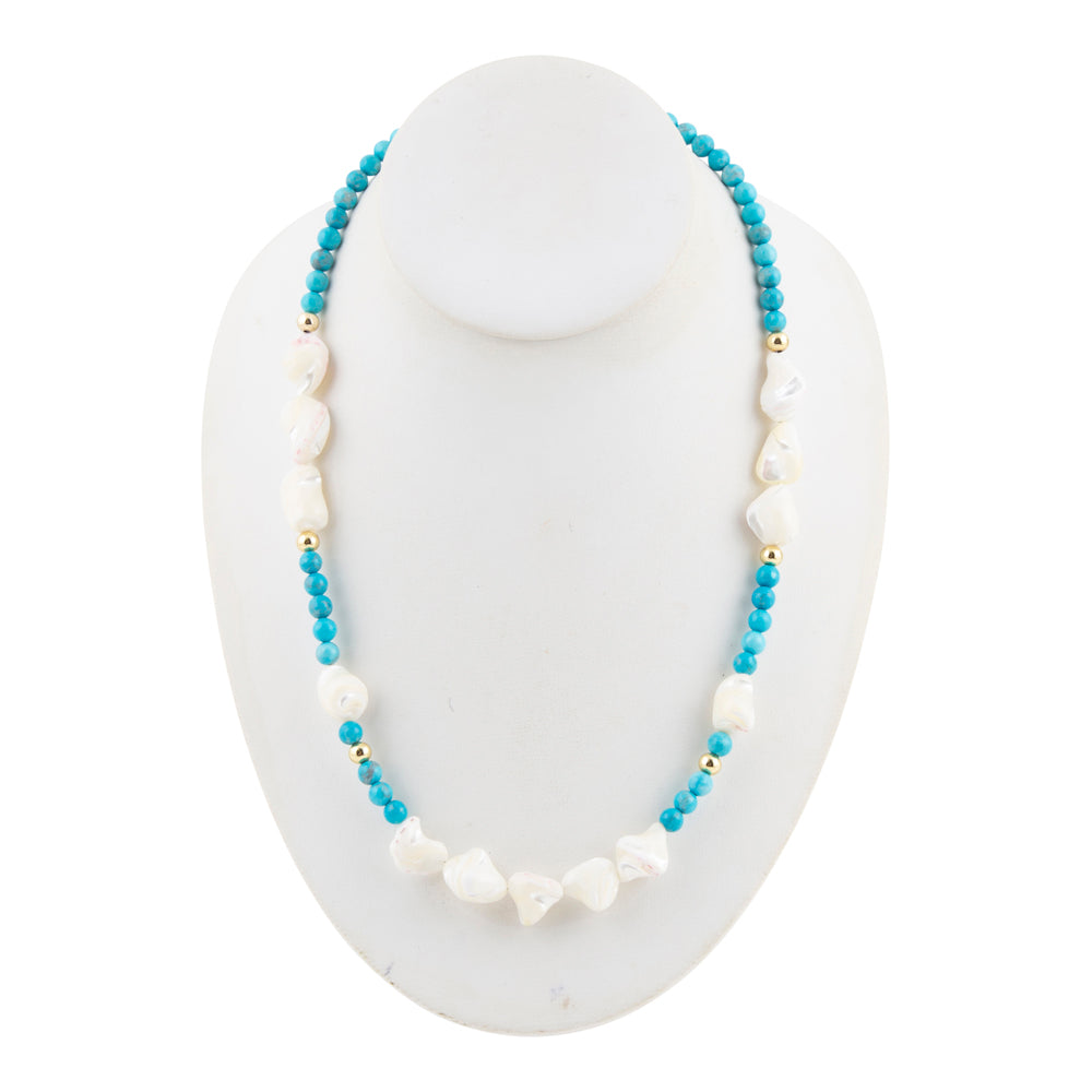 A beaded necklace displayed on a white mannequin bust, featuring light blue round beads, irregular white shell-like beads, and small gold spacer beads.