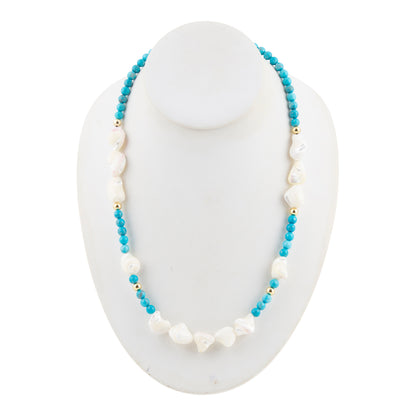 A beaded necklace displayed on a white mannequin bust, featuring light blue round beads, irregular white shell-like beads, and small gold spacer beads.