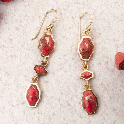 Gold earrings with red gemstones on a textured beige surface