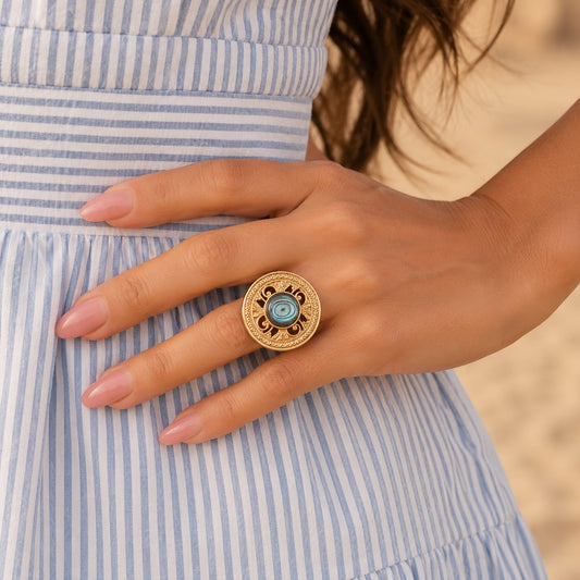 Close-up of a hand wearing a gold ring with a blue gemstone, against a blurred background.