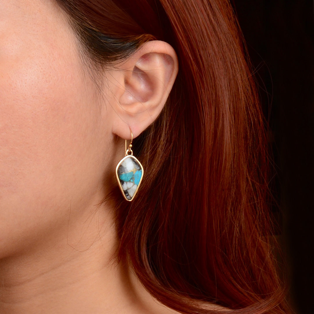 A close-up of a person's ear wearing a gold dangle earring with a marquise-shaped turquoise and white marbled stone.