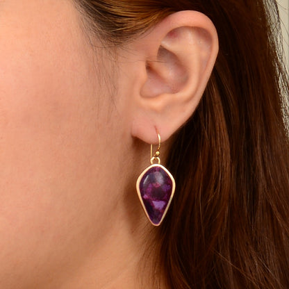 Close-up of an ear wearing a purple teardrop earring with gold setting.