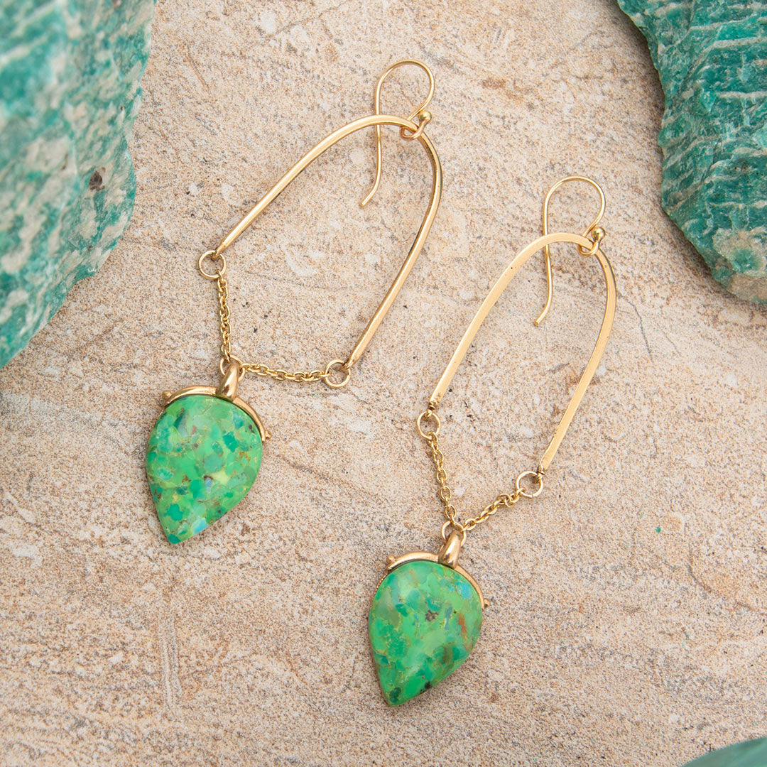 Gold earrings with green stone drops on a textured surface