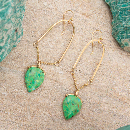 Gold earrings with green stone drops on a textured surface