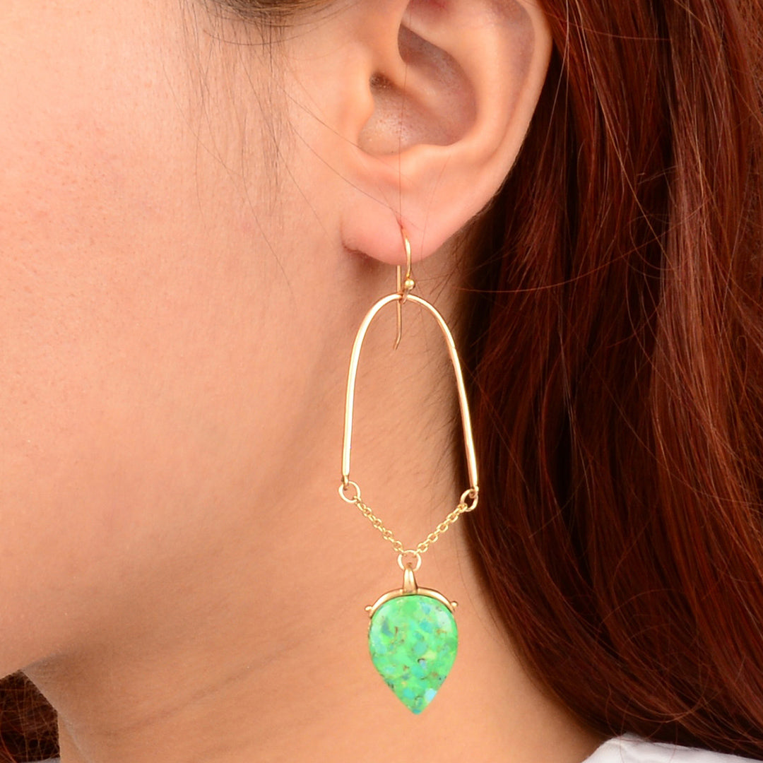 Gold earring with a green teardrop pendant worn by a person with red hair.