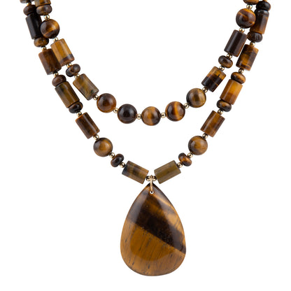 A double-strand beaded necklace made of polished tiger's eye beads in brown and black, featuring a large teardrop-shaped pendant with a matching tiger's eye pattern, set against a plain white background.