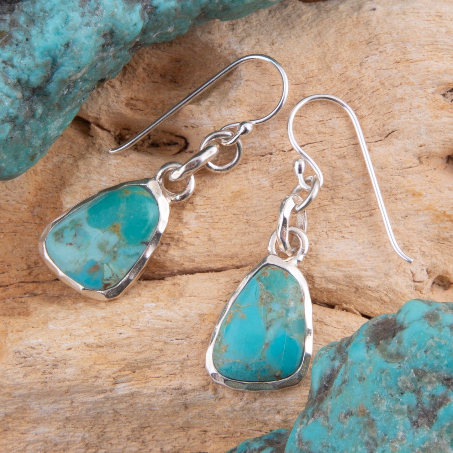 Turquoise teardrop earrings with silver hooks on a wooden surface with turquoise stones.
