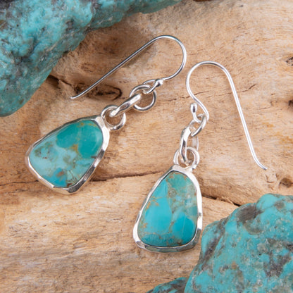 Turquoise teardrop earrings with silver hooks on a wooden surface with turquoise stones.