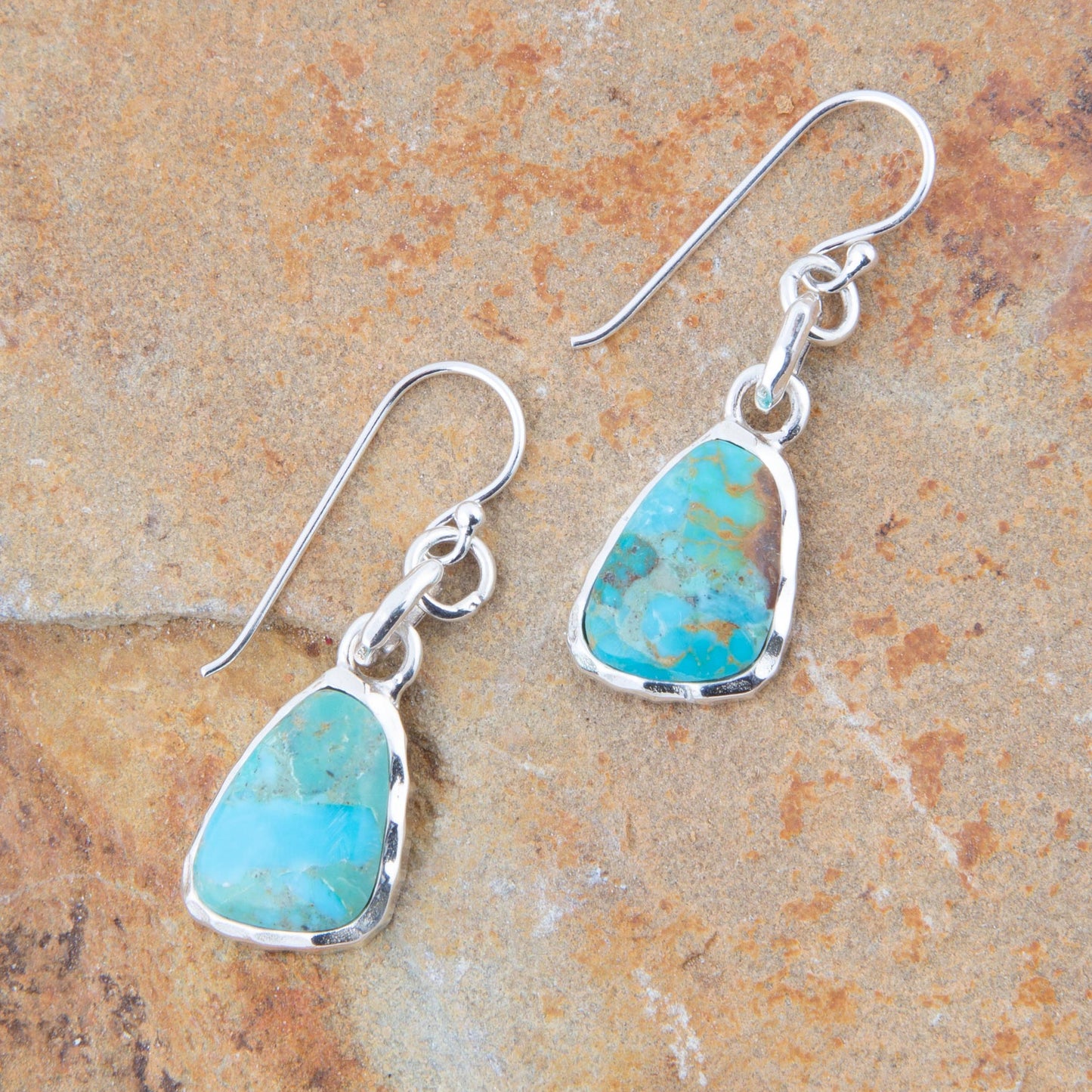 Turquoise teardrop earrings with silver hooks on a stone background