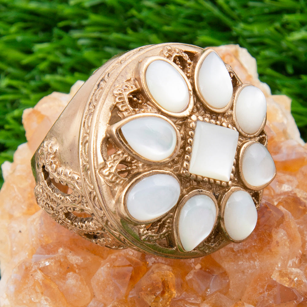 Gold ring with white stones on a textured surface with green grass in the background