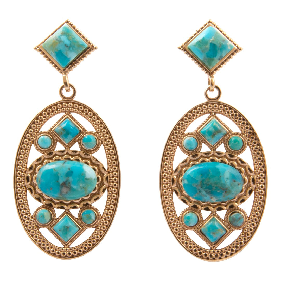 A pair of gold-toned statement dangle earrings featuring large turquoise-colored stones in a geometric filigree design, set against a plain white background.
