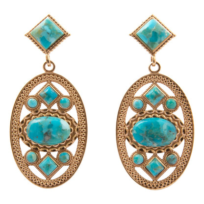 A pair of gold-toned statement dangle earrings featuring large turquoise-colored stones in a geometric filigree design, set against a plain white background.
