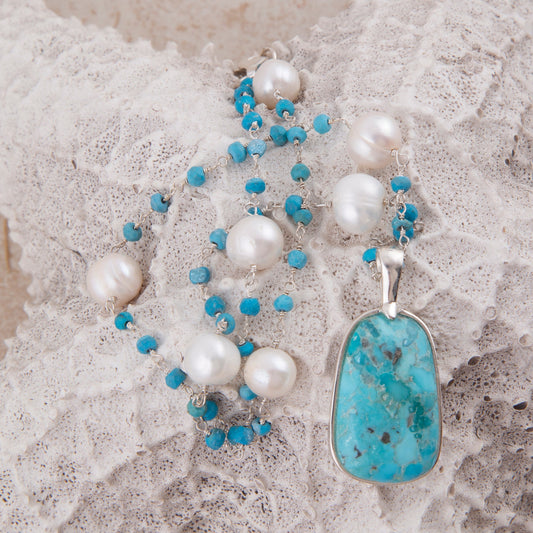 Necklace with pearls and a turquoise pendant on a textured surface
