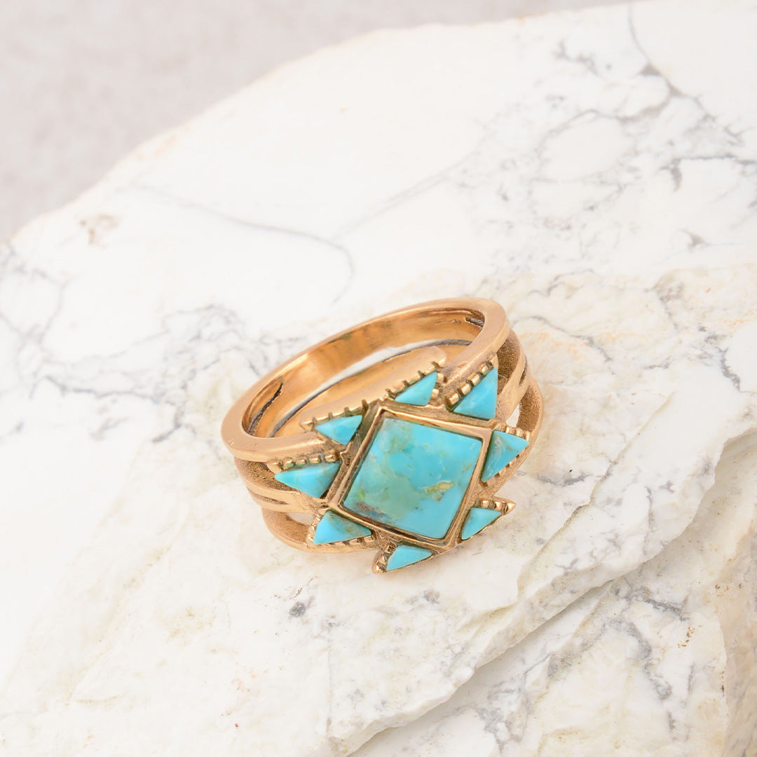 Gold ring with turquoise stone on a marble surface