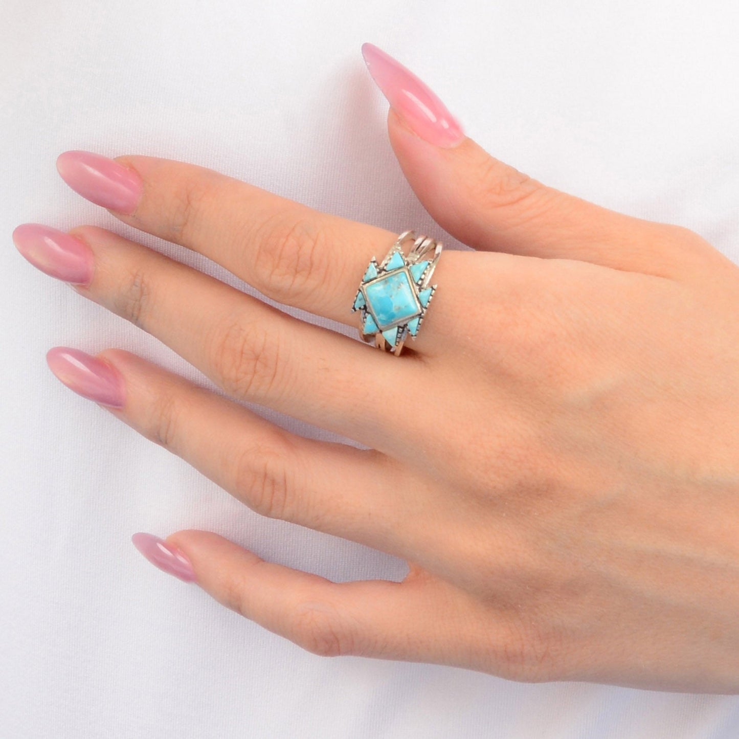 Hand wearing a turquoise ring with pink nail polish on a white background