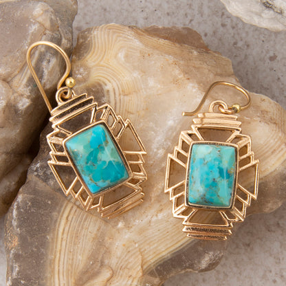 Gold earrings with turquoise stones on a stone background