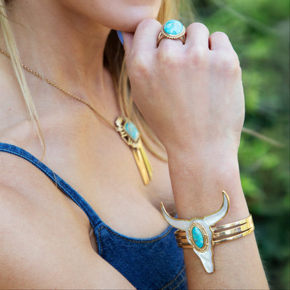 Woman wearing turquoise jewelry including earrings, ring, and bracelet with a blurred green background