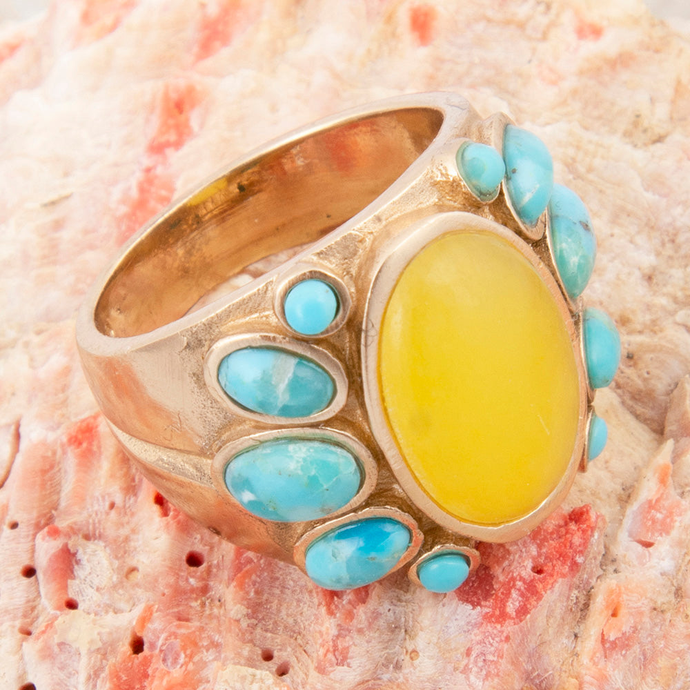 Gold ring with a yellow center stone and turquoise accents on a coral background
