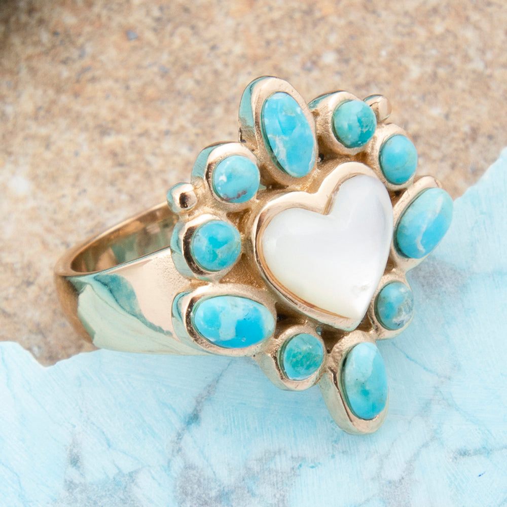 Gold ring with turquoise stones and a white heart on a textured surface