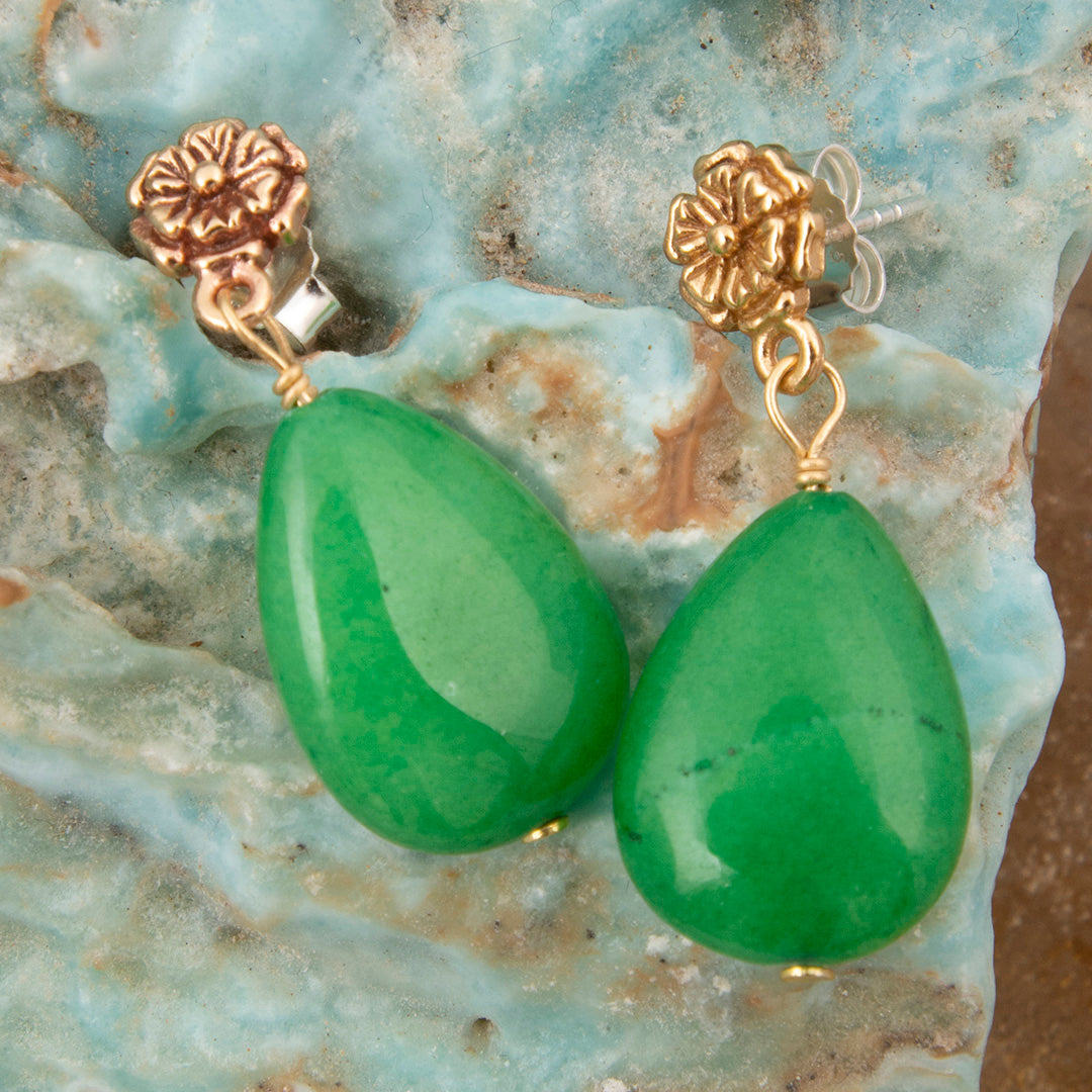Green teardrop earrings with gold hooks on a textured stone surface