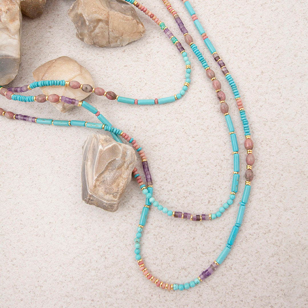 Beaded necklace with turquoise and multicolored beads on a sandy surface with rocks.