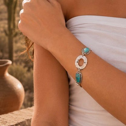 A close-up lifestyle shot of a woman wearing a silver-toned bracelet with two turquoise-colored stones on her wrist, wearing a white strapless top.