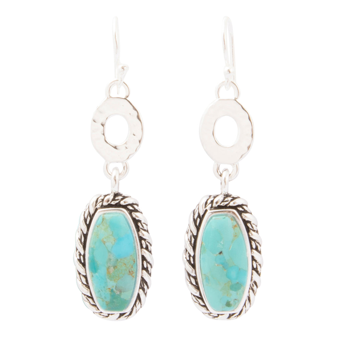 A pair of silver drop earrings featuring oval turquoise stone pendants with a textured rope border and a textured circular silver disc above, set against a plain white background.