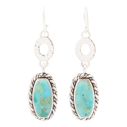 A pair of silver drop earrings featuring oval turquoise stone pendants with a textured rope border and a textured circular silver disc above, set against a plain white background.