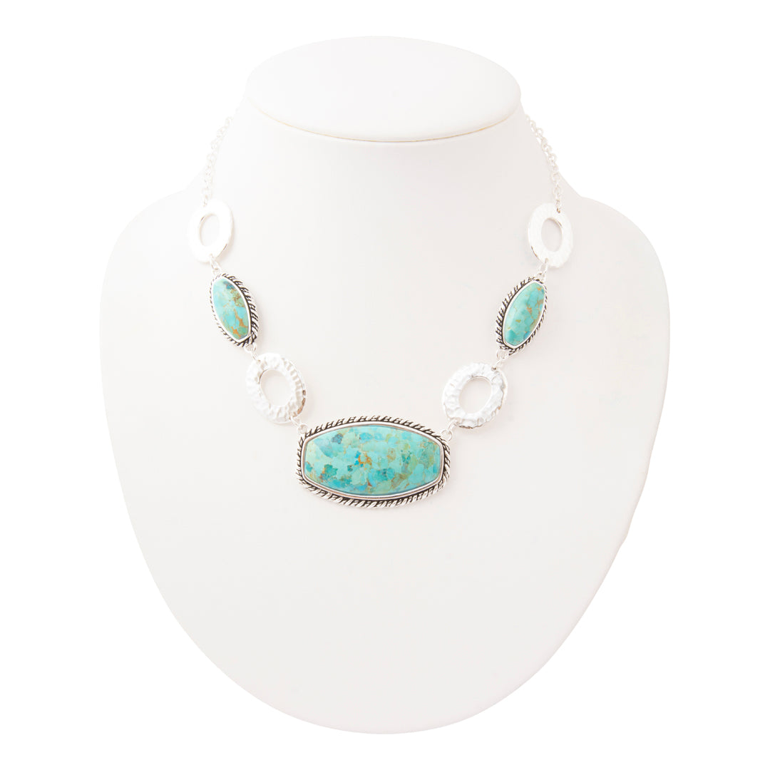 A silver-toned statement necklace with a large oval turquoise stone centerpiece and three matching turquoise stones, displayed on a white neck mannequin against a white background.